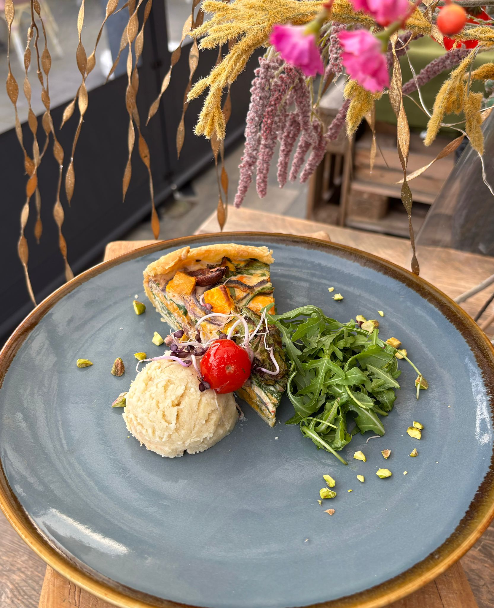Pompoen spinazie quiche – Grenzeloos Doldersum Pompoen-spinaziequiche met rucola, puree en een cherrytomaat, geserveerd bij Grenzeloos in Doldersum, Drenthe.