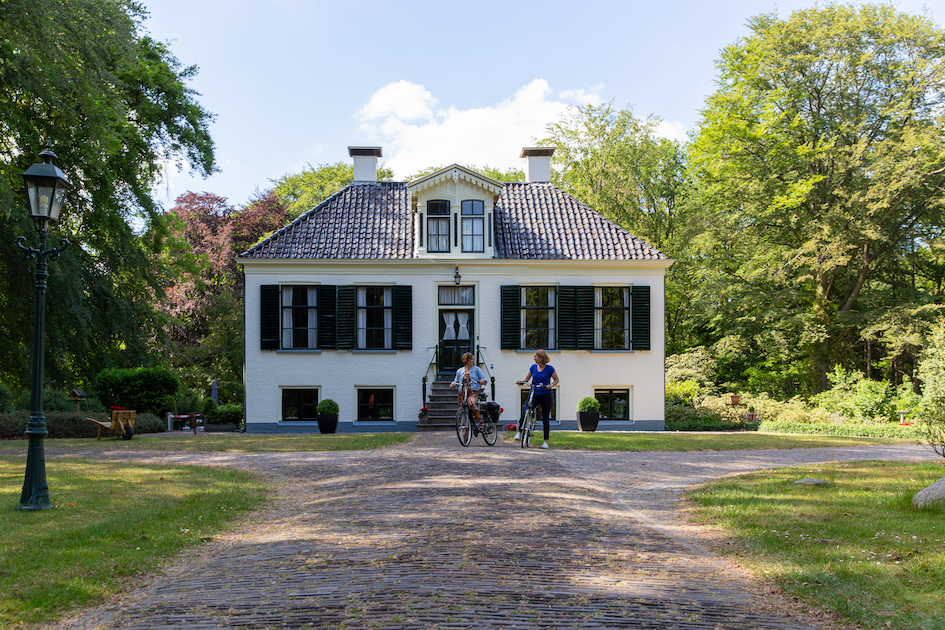 Twee fietsers voor een historisch huis in de Koloniën van Weldadigheid