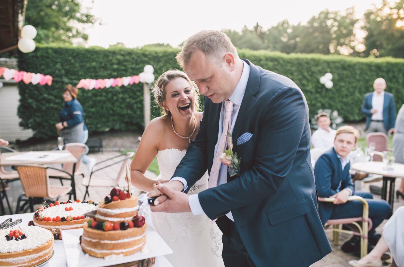 Bruid en bruidegom snijden samen de bruidstaart aan tijdens een buitenbruiloft